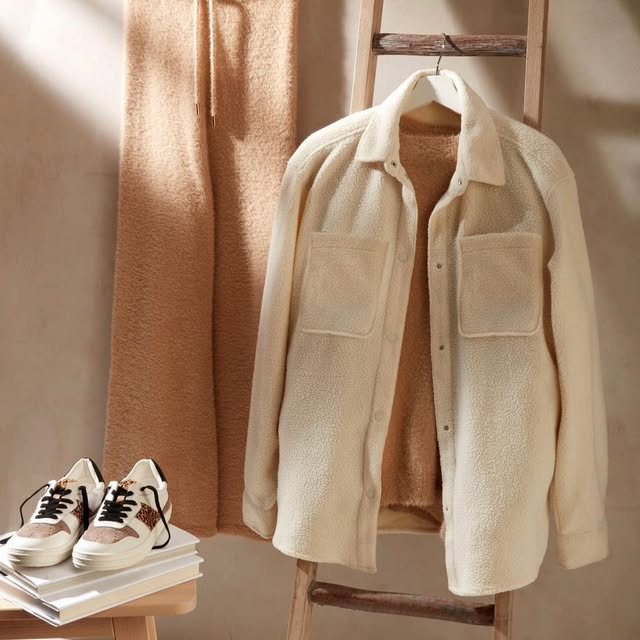 Cream fleece overshirt hung on a wooden ladder beside a camel throw