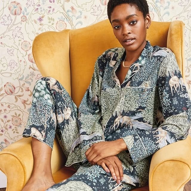 Woman in a woodland-print satin pyjama set, seated in a yellow armchair
